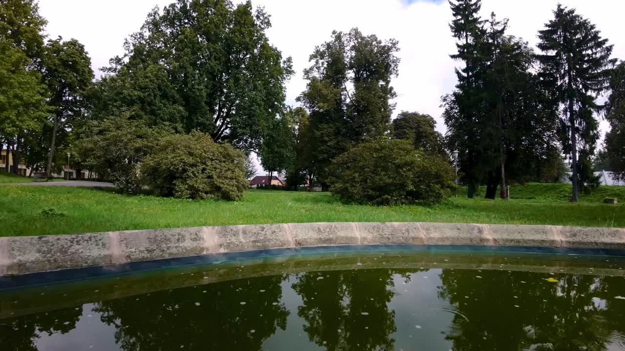 un dron se disparó hacia adelante sobre una antigua fuente en un parque cubierto de exuberante vegetación durante el día.