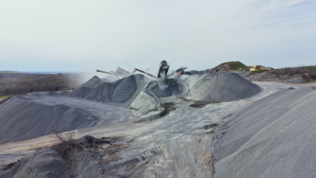 Granite quarry activity with large piles of stone and machinery working on a cloudy day
