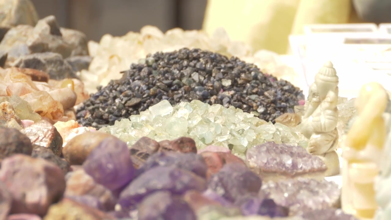 Ametista roxa bruta e pilhas de pedras semipreciosas não lapidadas no Mercado de Gemas de Chanthaburi em Chanthaburi, Tailândia. Plano inclinado para baixo, com foco se ajustando