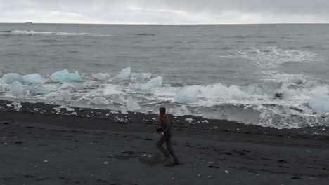 aerial shot following young man running along a cold beach