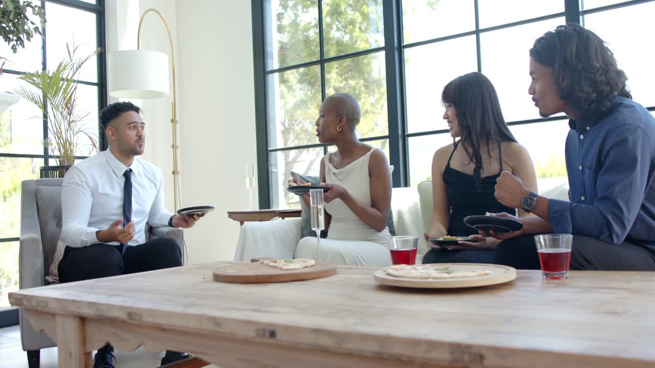 Diverse friends sitting on sofa, left man speaking, passing cup to woman tasting food while sharing
