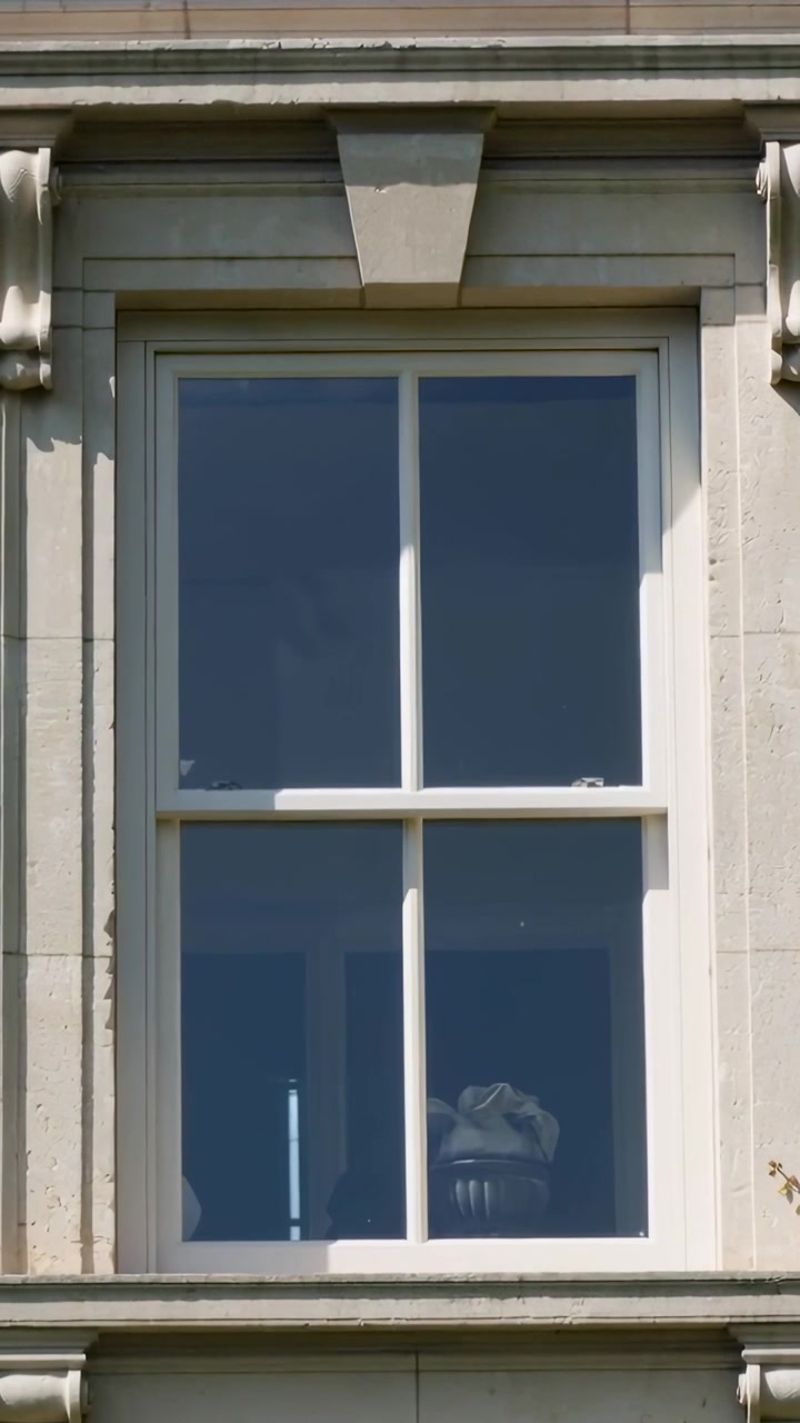 Vertical video: Zooming camera filming four-pane window on stone facade, revealing mask and lamp