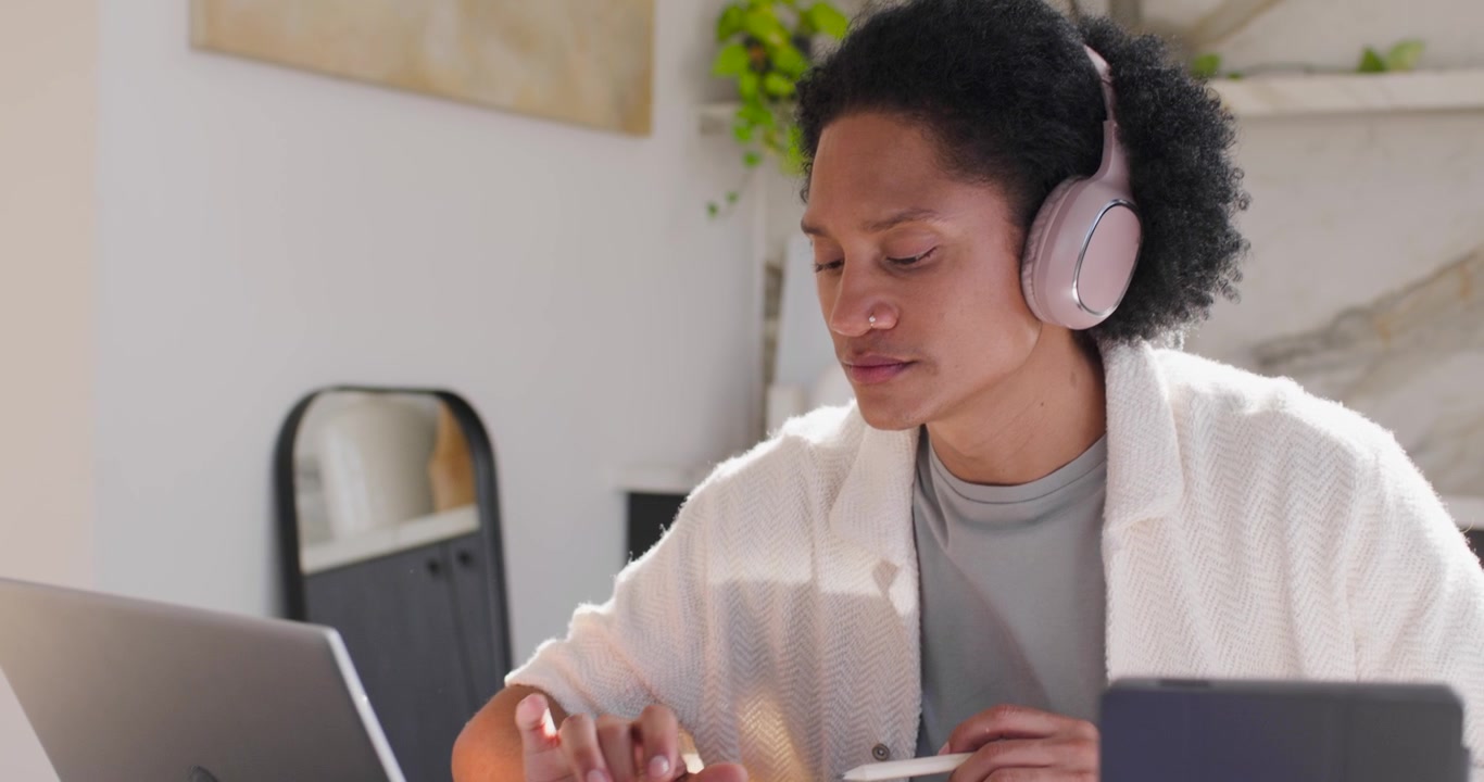Afroamerikanischer Mann hört mit rosa Kopfhörern zu, tippt auf einem Laptop und verwendet einen Stylus für die Arbeit zu Hause.