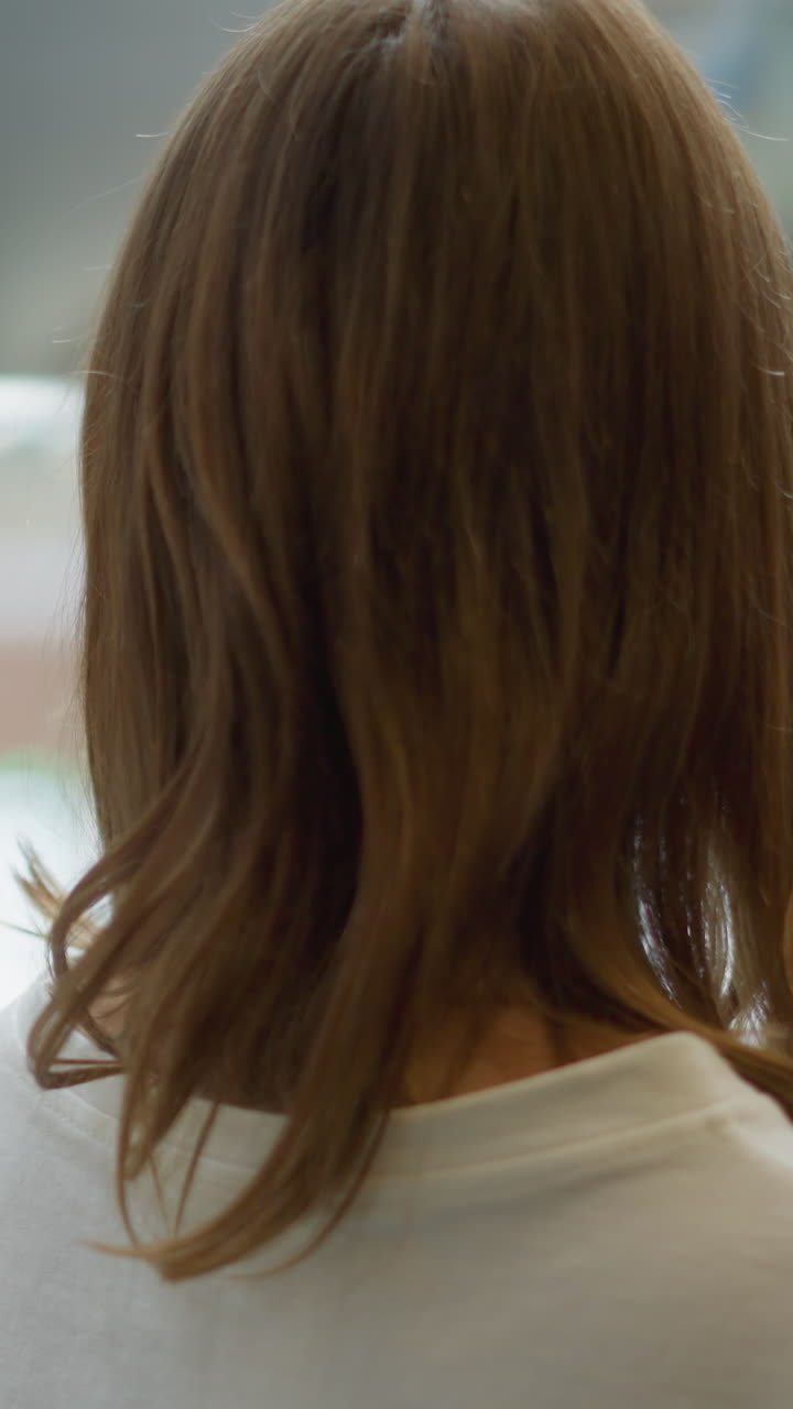 유리 패널을 통해 도시 환경을 흐릿하게 볼 수 있는 부드러운 자연 조명으로 움직이는 엘리베이터 안의 젊은 여성의 뒷면