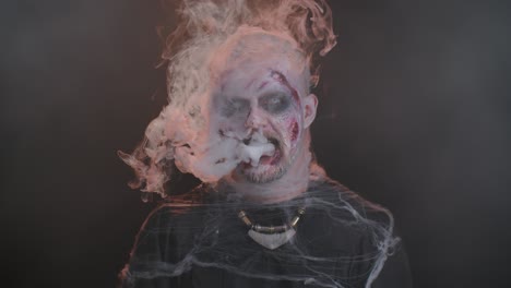 sinister man horrible scary halloween zombie looking ominous at camera blows smoke from nose, mouth