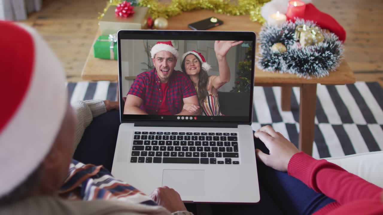 madre y hija afroamericanas usando una computadora portátil para una videollamada de navidad con la pareja en la pantalla