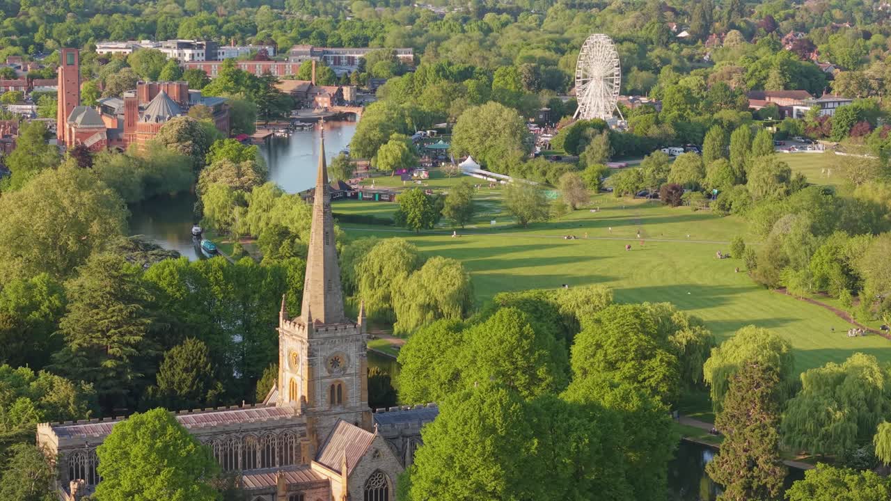 Imagem de drone focando na Igreja Gótica da Santíssima Trindade, inclinando-se para cima ou passando pelo pináculo para revelar uma vasta paisagem primaveril florida no horizonte de Stratford-upon-Avon.