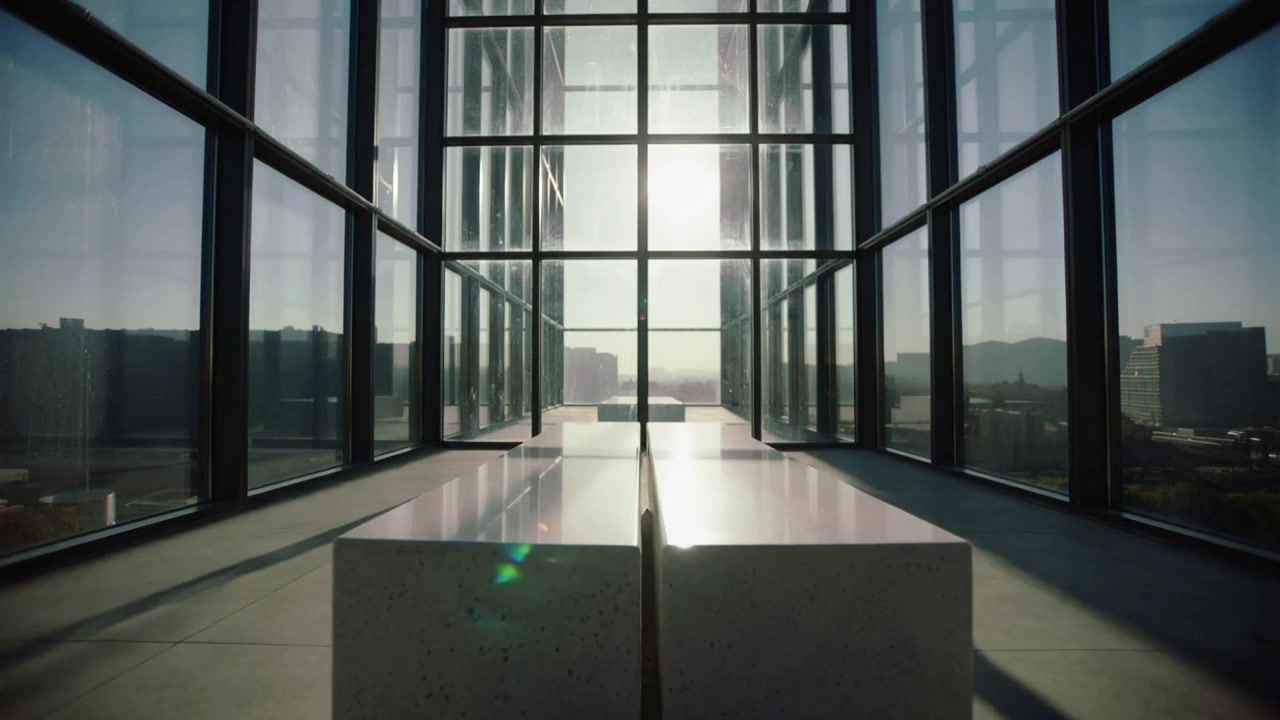Cámara avanzando en un atrio, revelando bancos brillantes que se reflejan en paredes de cristal para mostrar la luz.