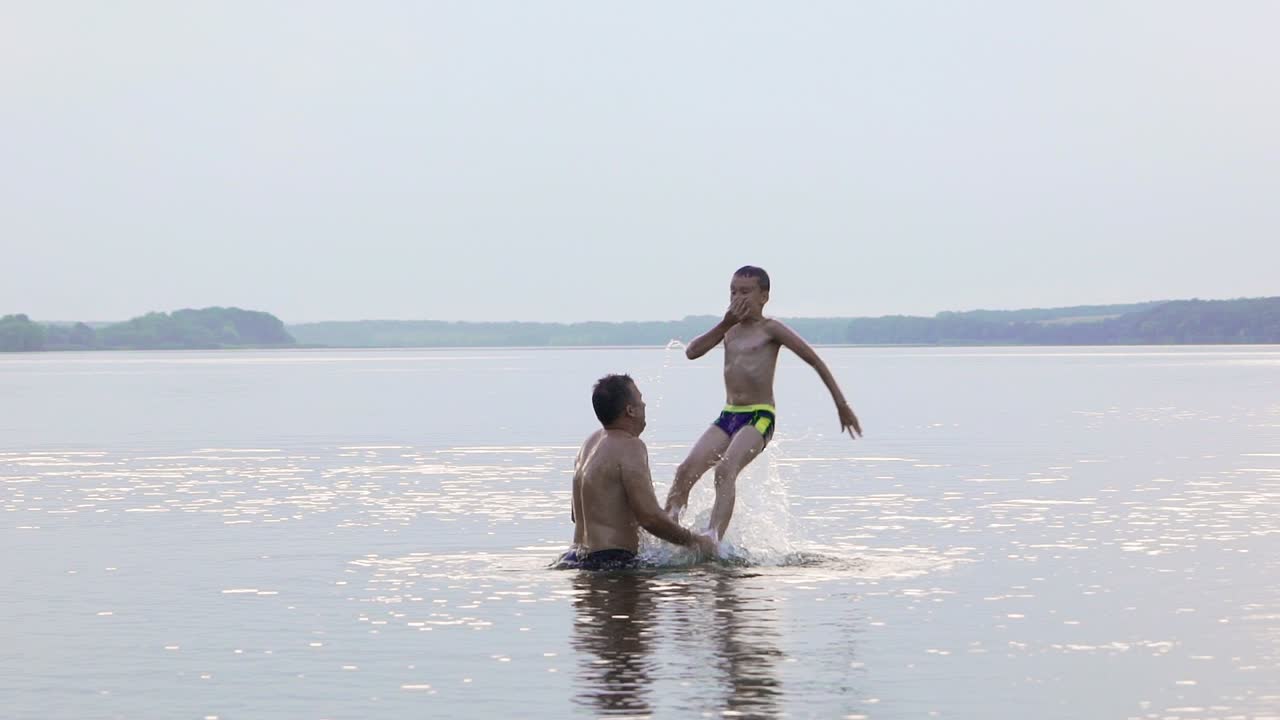 Happy family. Father and son are having fun and splashing in the water. Slow motion.