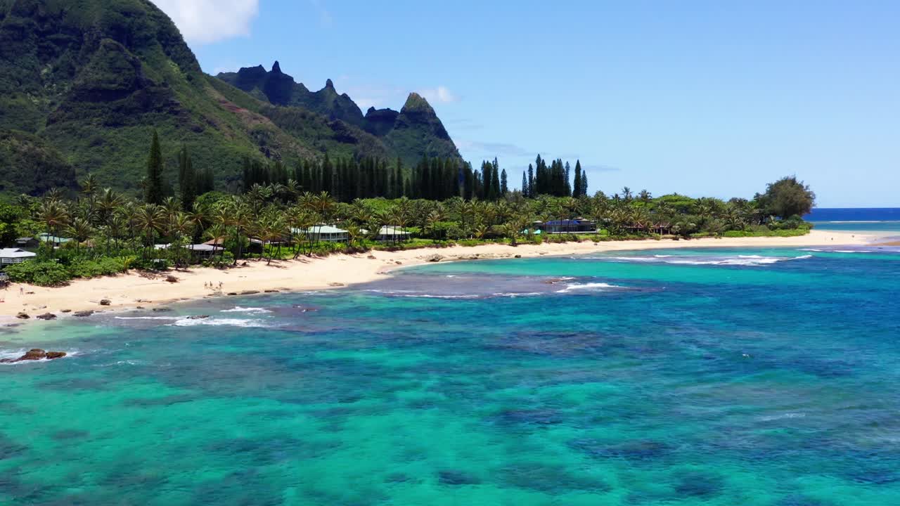 Smooth 4K aerial of Tunnels Beach in Kauai, Hawaii. Clear ocean water reveals reef patterns. Lush rainforest mountains complete this tropical, cinematic view