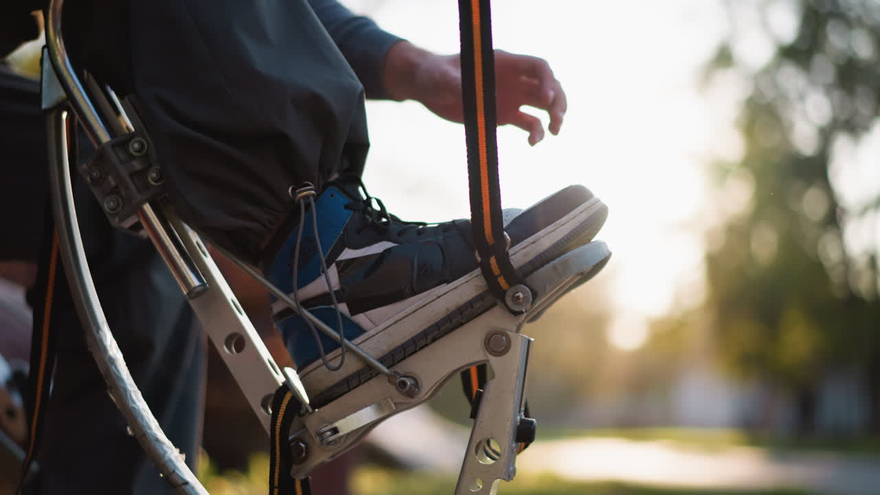 야외에서 활 기 장비에 을 조정하는 젊은 남자의 손의 클로즈업. 그는 부드러운 빛을 비추는 장면과 함께 회색 후디를 입고 있으며, 배경에는 흐릿한 초록색이 있습니다.