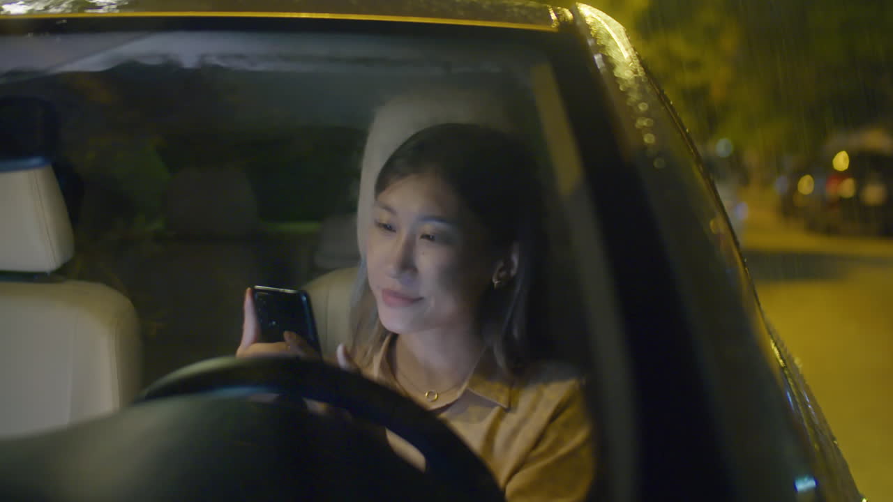AsianWoman Using Phone in Car at Rainy Night