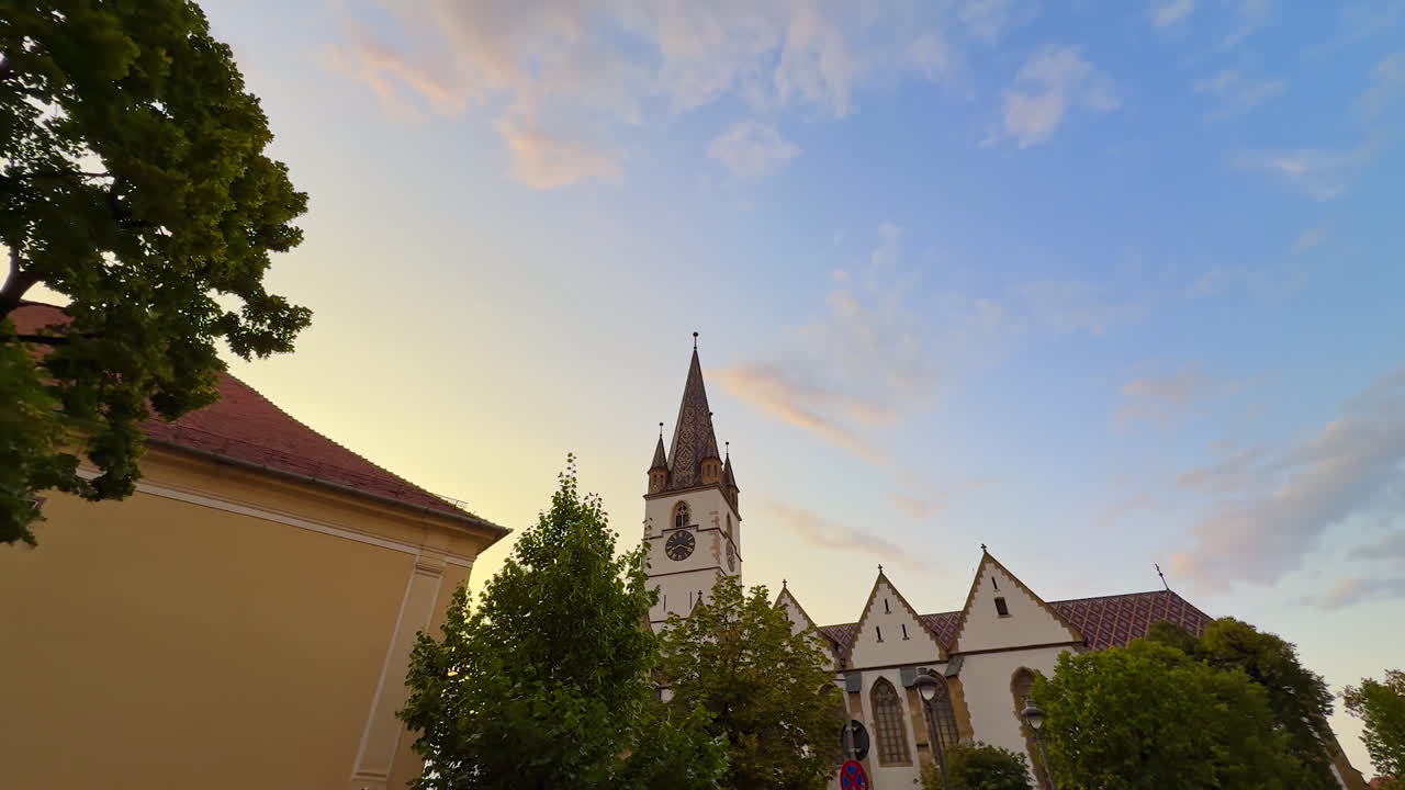 Church spire and sunset sky in Sibiu. A tall Gothic church spire rises above the trees in Sibiu, Romania, against a colorful evening sky with clouds and soft light