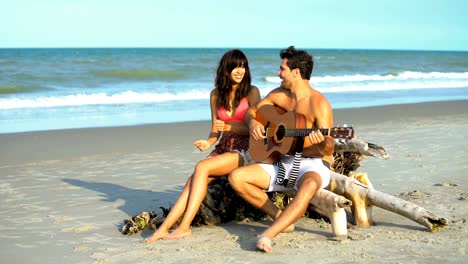 smiling multi ethnic couple in swimsuits playing guitar