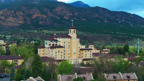 drone establishing telephoto orbit glides over broadmoor resort, green trees and lake below under clear sky