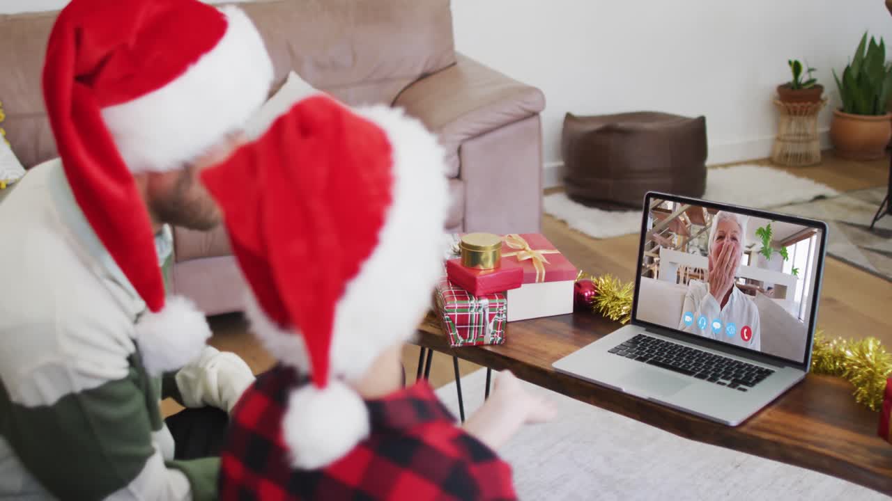 padre y hijo caucásicos usando sombreros de santa en una videochat portátil durante la navidad en casa