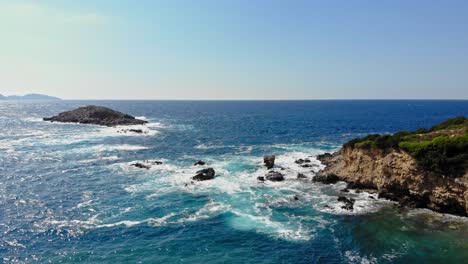 Blaue-Ozeanwellen,-Die-Gegen-Die-Felsigen-Klippen-Und-Das-Ufer-Am-Strand-Von-Jerusalem-In-Griechenland-Prallen---Drohnenaufnahme-Aus-Der-Luft