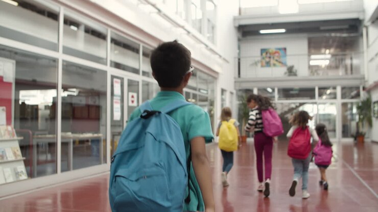 Plano medio de un niño caminando por el pasillo de la escuela detrás de sus compañeros de clase