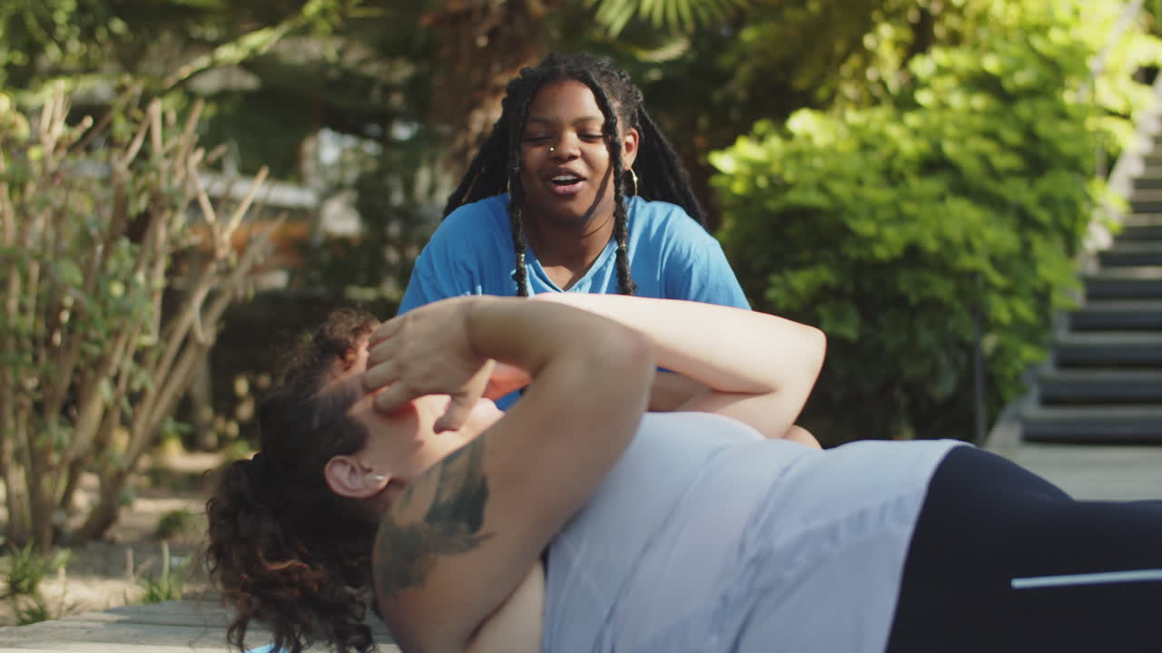 una chica afroamericana animando a su amiga que hace ejercicio abdominal