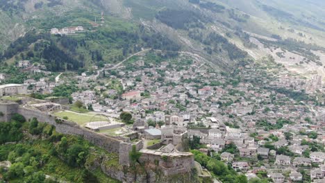 Drohnenansicht-In-Albanien,-Die-In-Der-Stadt-Gjirokaster-über-Eine-Mittelalterliche-Burg-Auf-Einer-Hochgelegenen-Festung-Fliegt-Und-Die-Ziegelbraunen-Dachhäuser-Zeigt