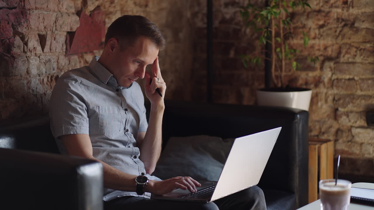 retrato en primer plano de un joven reflexionando en la oficina. el diseñador planea su trabajo y sostiene un lápiz en su mano. el disparo es en cámara lenta desde abajo. hombre serio pensativo sentado con una computadora portátil pensando solución