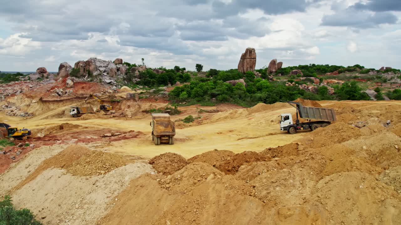 Sand dump area in construction site with trucks, trees, rocks and clouds on sky at telangana, india. day time, semi orbit, drone shot, 4k.