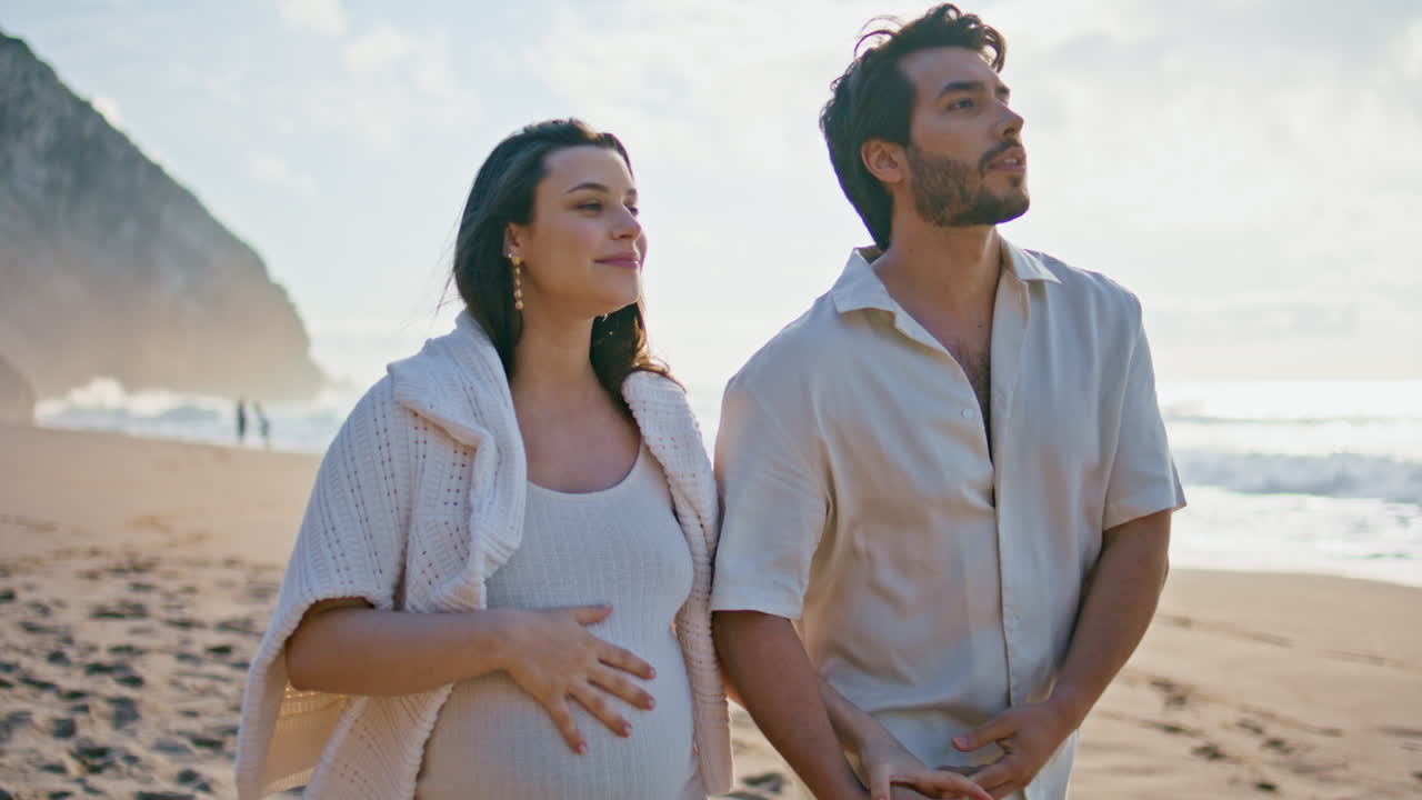 남자가 빛 해변에서 임신한 아내를 고 있다. 남편이 여자의 손을 키스하고 있다.