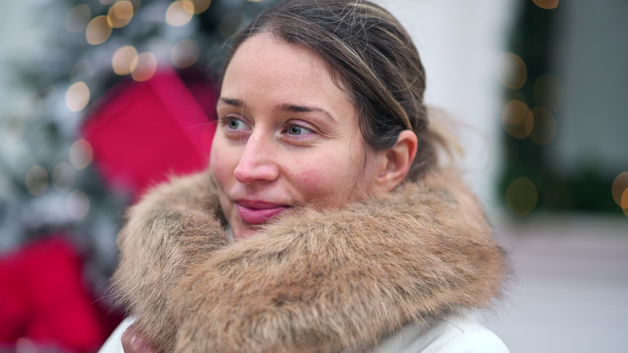 A woman enjoys outdoor festivities, wearing a warm fur scarf. She smiles warmly while surrounded by holiday decorations and a cheerful atmosphere in the city
