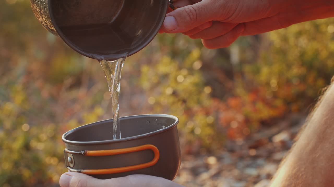 Pouring water into a metal cup outdoors