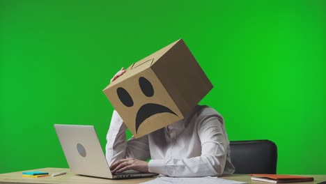 person with a box on their head, working on a laptop