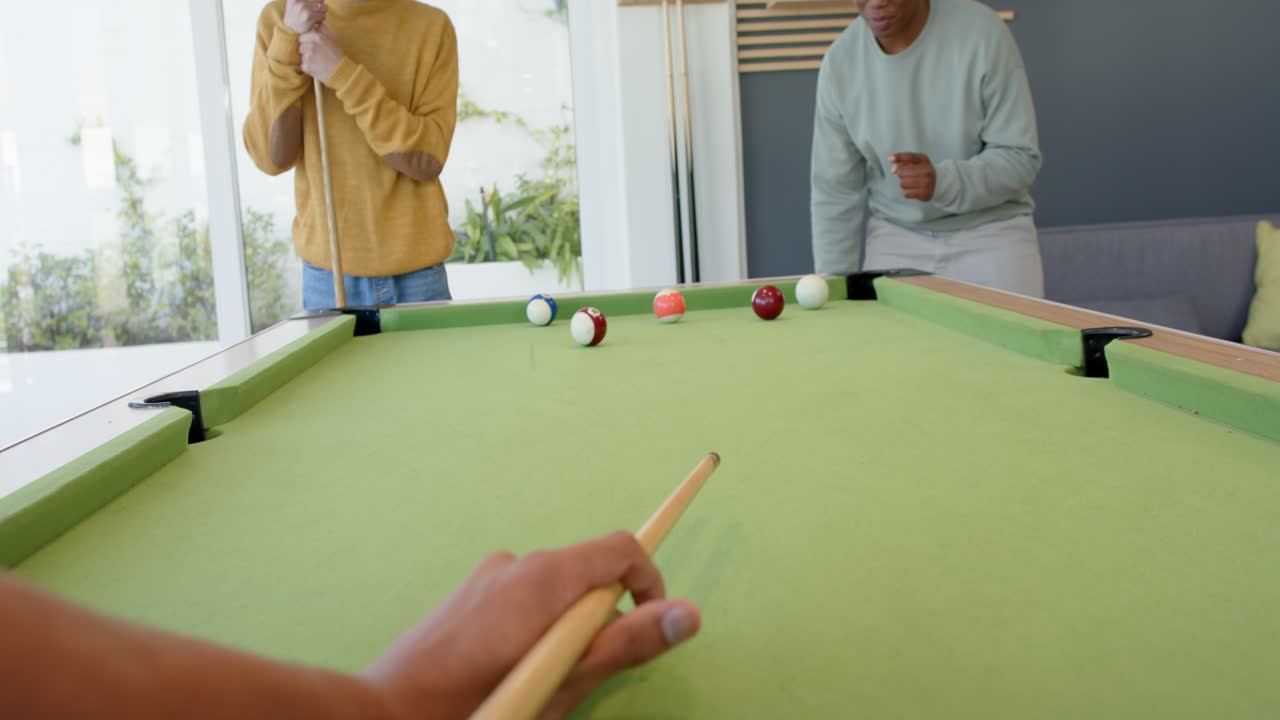 Shooter aligning cue, shooting white ball across pool table at home while friends celebrating win