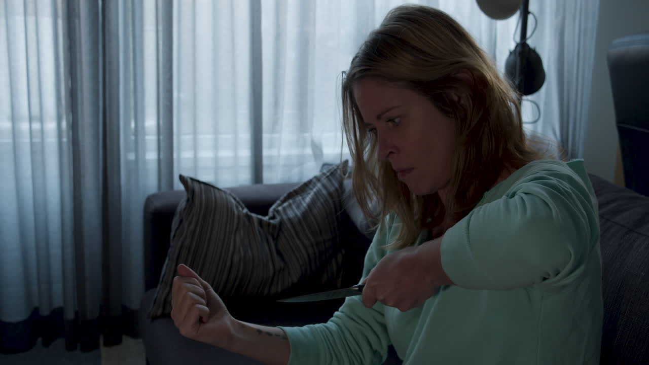 거실에서 우울한 여자가 칼로 손목을 잘라 자살을 시도하다