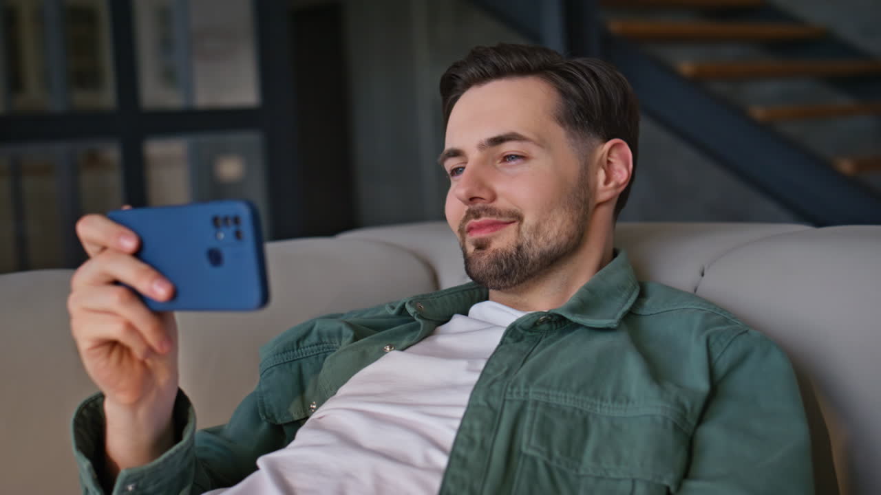 Online guy lying couch with smartphone taking rest closeup. Smiling man relaxing