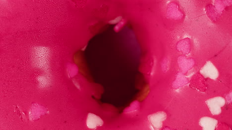 close-up of a pink glazed donut with heart sprinkles