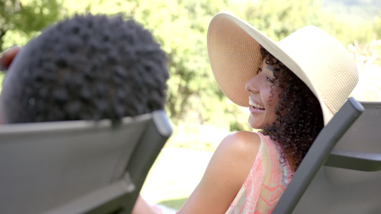 Relaxing outdoors, woman in sun hat smiling while sitting on lounge chair