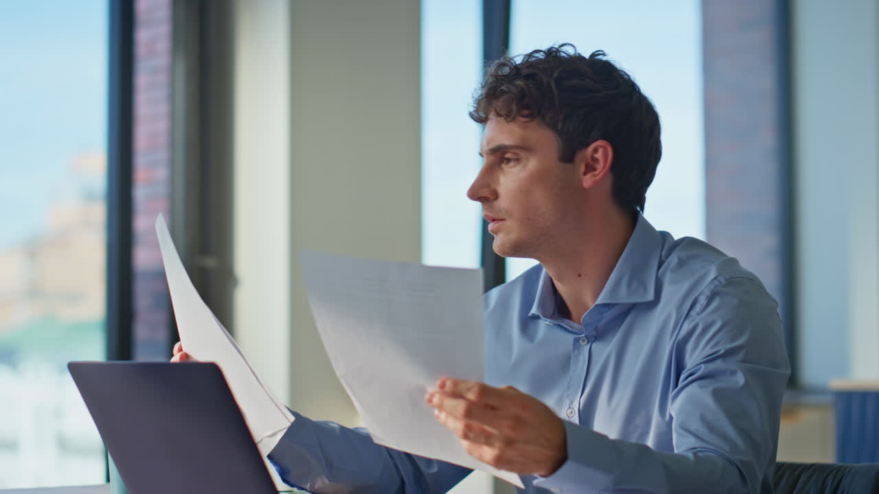Busy businessman reviewing papers working in home office with laptop closeup