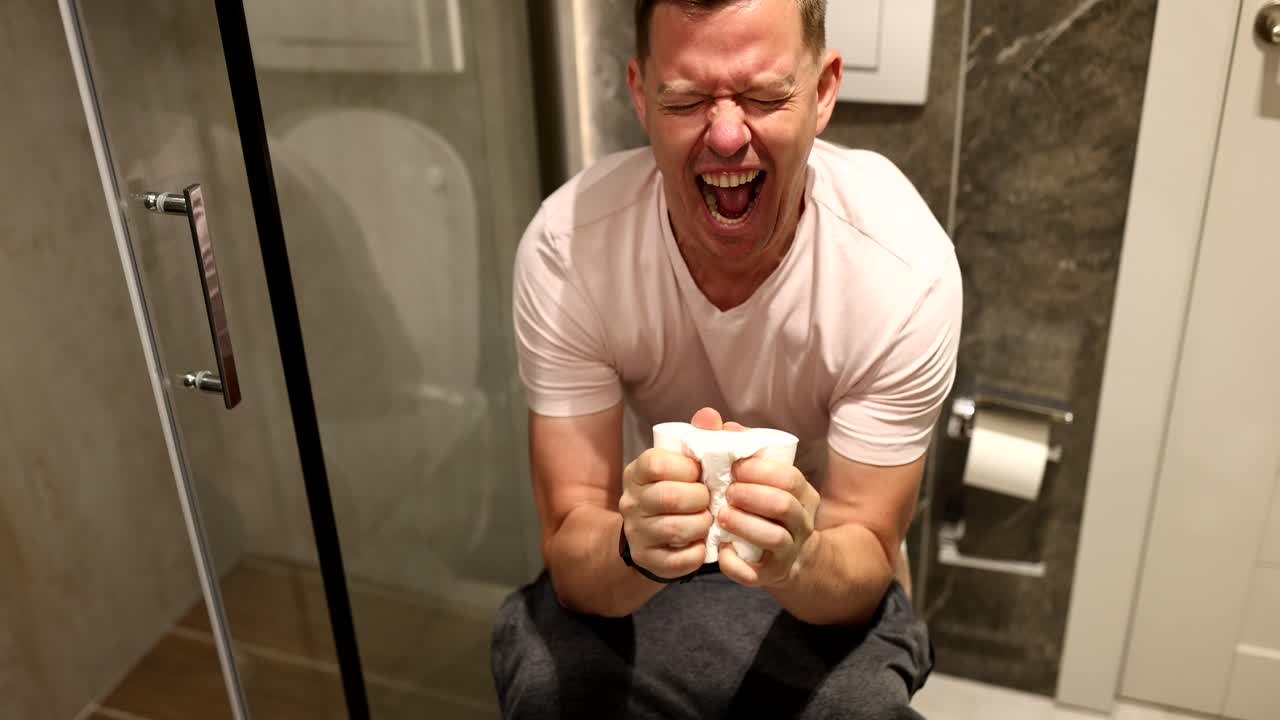 Man sits on toilet with toilet paper and suffers from constipation