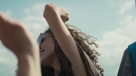 camera tracking smiling young caucasian woman with curly hair dancing at music festival among friends