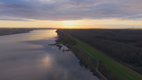 aerial view of a river at sunset, with golden light reflecting on the water and a forested shoreline. dutch landscape.