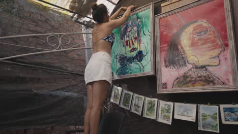 an indian girl hanging a painting in an art gallery