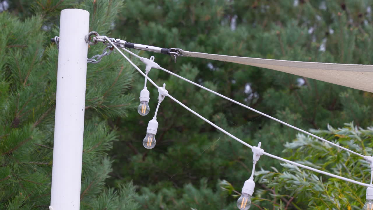 Decorative string lights hang from a white post with green pine trees in the background creating a cozy outdoor atmosphere