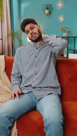 man sitting on a red couch, holding his neck in pain