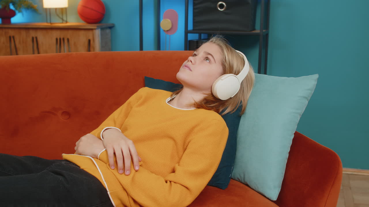 소년은 소파에 누워서 무선 헤드폰으로 오디오북을 듣고 집에서 언어를 배우고 있습니다.