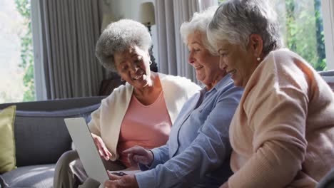 three diverse senior women using laptop together sitting on the couch at at home