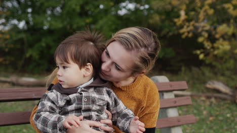 a young mother with a little son sits on a bench in the park