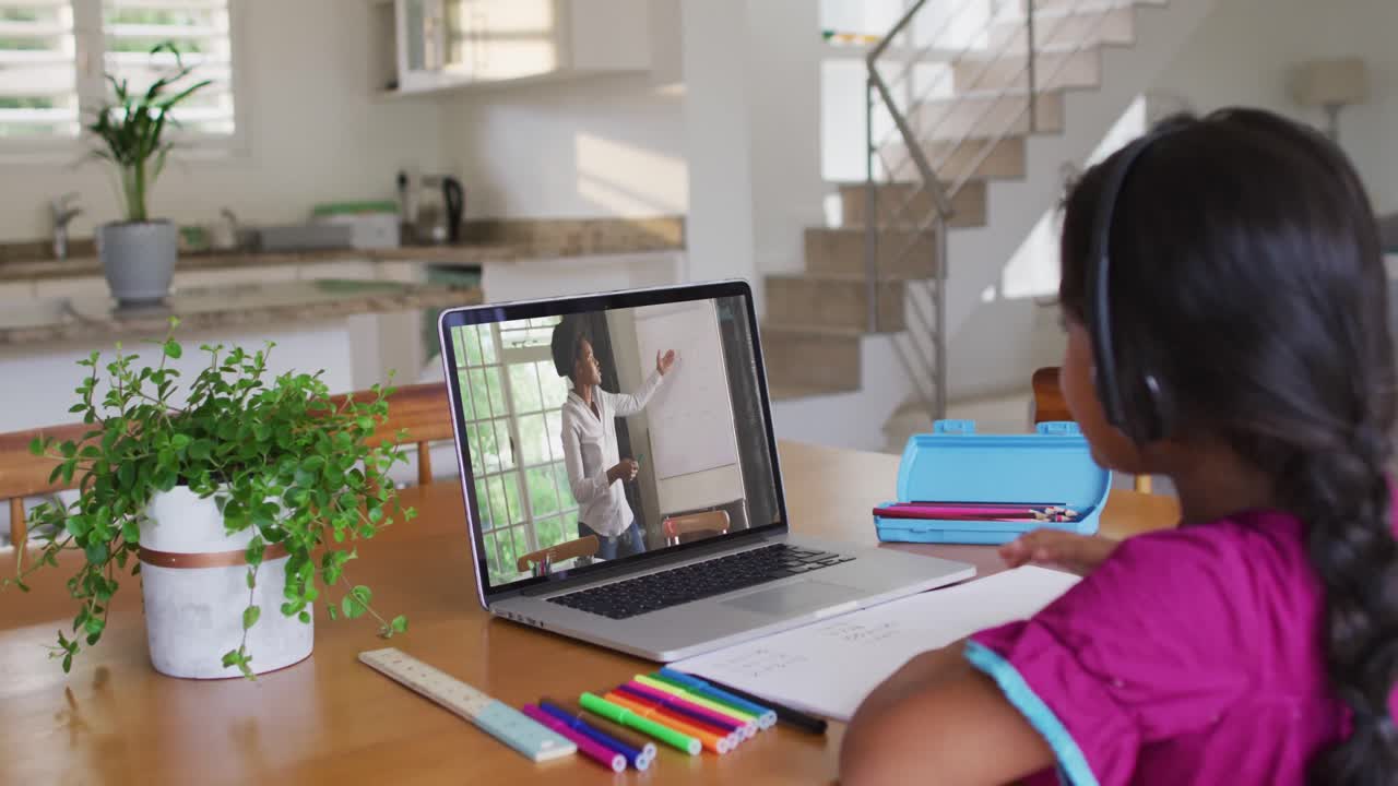 chica afroamericana haciendo la tarea mientras tiene una videollamada con una maestra en una computadora portátil en casa
