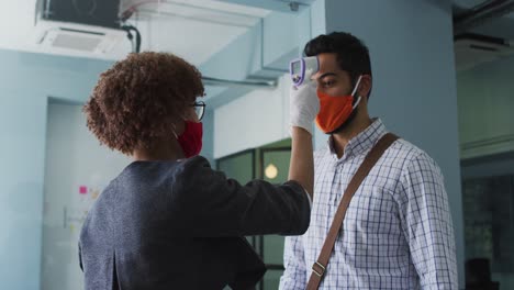 african american woman wearing face mask measuring of her male colleague at modern office