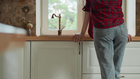 woman leans on countertop by kitchen sink closeup housewife rests looking out of window after dishes