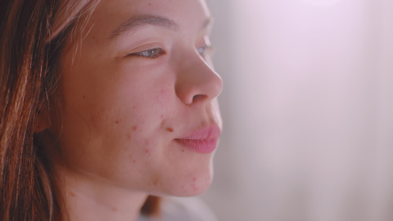Close up of young girl eating cheese layered snack with cucumber slice, focused expression showing detail of bite, natural indoor light highlighting face and hands