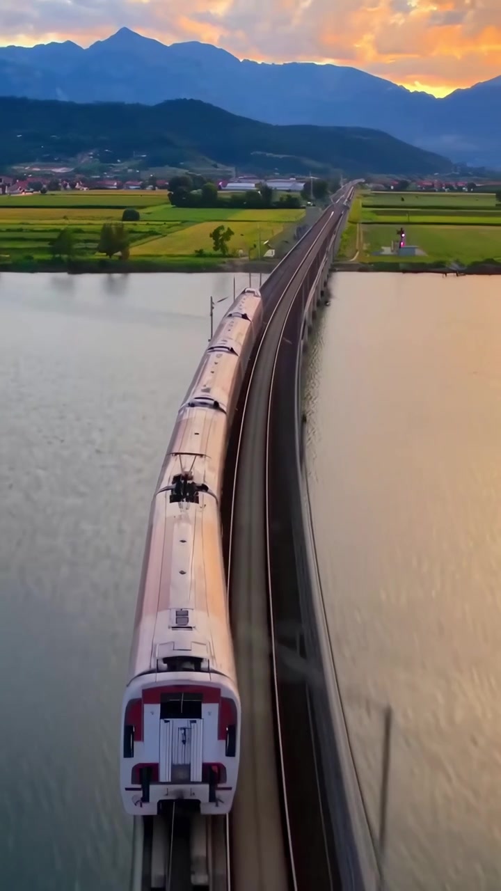 Kereta Cepat Melintasi Pemandangan Pedesaan yang Indah dan Jembatan saat Matahari Terbenam